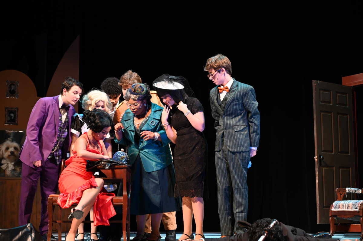 Members of the cast huddle around Izzy Blackledge (12), who played Miss Scarlett, as they devise a plan. Blackledge did an excellent job of portraying Miss Scarlett's intelligence (as seen in this scene) as well as the more flirtatious aspects of her character. 