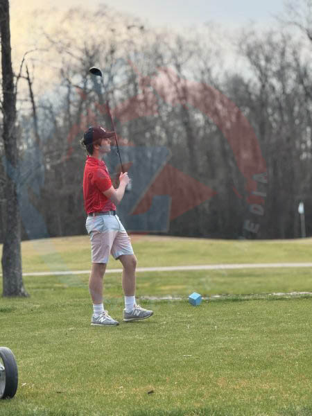 Tucker Cox (10) watches as his opponents play before him, golf club in hand.